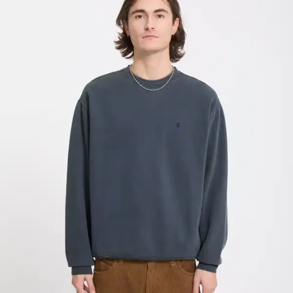 Männlicher Model trägt einen Vintage Storm Blue Pullover von Volcom, kombiniert mit braunen Hosen, auf neutralem Hintergrund.