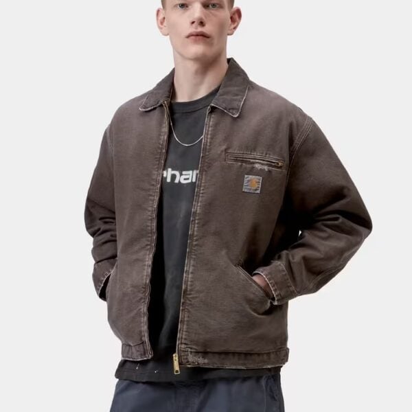 Männlicher Model trägt die Carhartt Wip OG Detroit Canvas Jacke in braun, kombiniert mit dunklen Hosen, auf weißem Hintergrund.