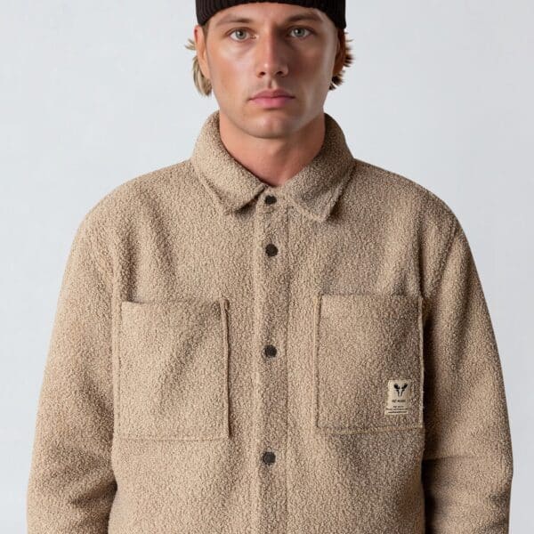Mann trägt Fat Moose ACE Overshirt in Sandfarbe, kombiniert mit schwarzem Beanie, moderner Streetwear-Look, Fokus auf Komfort und Stil.