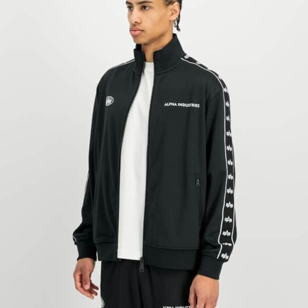 Mann trägt schwarze Alpha Industries Track Tricot Jacke mit weißen Logos und Streifen, sportliches Outfit, modisch und bequem.