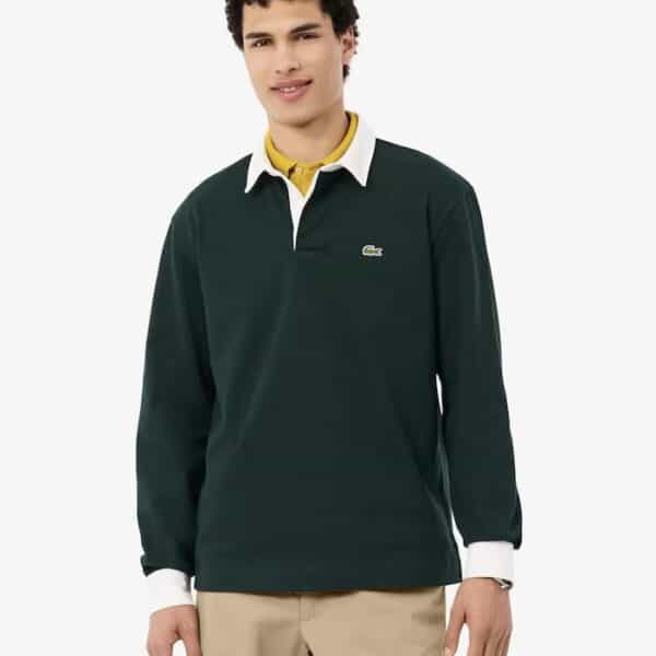 Junger Mann trägt ein grünes Lacoste Rugby Polo Langarmshirt mit weißem Kragen und Logo, kombiniert mit beige Hosen, vor weißem Hintergrund.