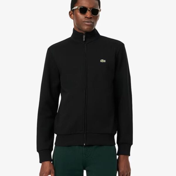 Mann trägt schwarze Lacoste Sweat Track Jacke mit Reißverschluss, Sonnenbrille, und grünen Hosen, stilvoll und sportlich.