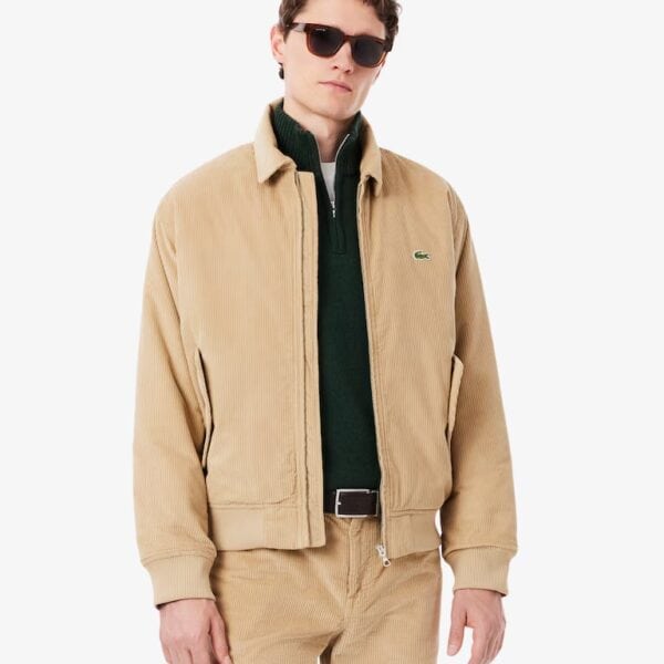 Mann trägt beige Lacoste Oxford Cord Winterjacke mit Reißverschluss, Sonnenbrille und dunklen Sonnenbrille, stilvoller Winterlook.