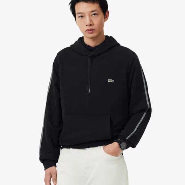 Mann trägt schwarzen Lacoste Kapuzenpullover mit Reißverschluss und Logo-Details, casual Look, Mode für Herren.