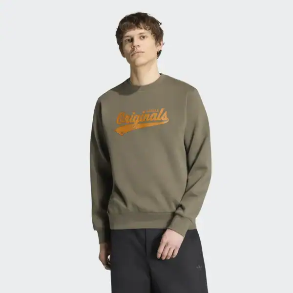 Mann trägt einen grünen Adidas Originals Pullover mit orangefarbenem Logo, lässig in einem Studio fotografiert.