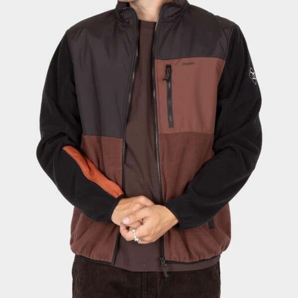 Männliche Person trägt die Iriedaily Flecce Jacke in Dunkelbraun mit schwarzen und orangefarbenen Akzenten, ideal für den Herbst.